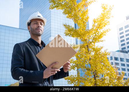 Erfahrener Architekt, Bauingenieur in weißem Schutzhelm. Moderne Gebäude im Hintergrund Stockfoto