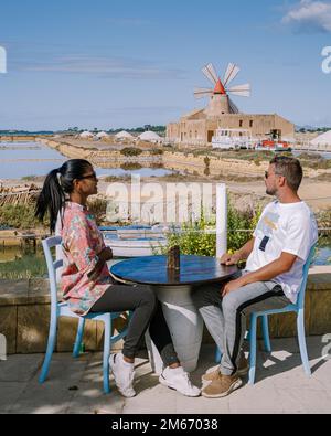 Ein Paar trinkt Kaffee mit Blick auf die Windmühle und Salinen in der Nähe von Marsala, Sizilien, Italien, Männer und Frauen im Urlaub in Sizilien Stockfoto