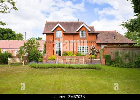 Großes englisches Landhaus und Garten im Sommer mit Rasen und Terrasse mit Teakholzgartenmöbeln Stockfoto