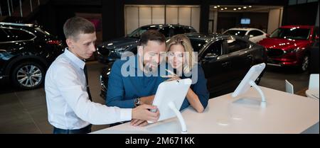 Kaukasisches Ehepaar wählt ein Auto in einem Autohaus auf digitalen Tablets. Stockfoto