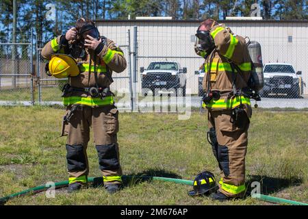 Ethan Harris, Left, und Richard Miller, Right, beide Feuerwehrleute aus Camp Lejeune Fire and Emergency Services, legen ihre Gasmasken an, bevor sie eine Flughafen-Feuerwehr praktizieren, auf der Marine Corps Basis Camp Lejeune, North Carolina, 9. April 2022. Alle Mitarbeiter von Camp Lejeune Fire and Emergency Services müssen eine Feuerwehrzertifizierung am Flughafen erhalten, um jede Mission an Bord der Marine Corps Air Station New River zu unterstützen. Stockfoto