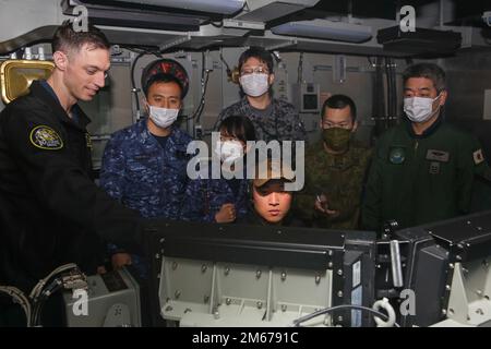 220410-N-DF558-2009 OSTCHINESISCHES MEER (10. April 2022) LT. Corby Bivans, links, aus Las Vegas, Und Chief Logistics Specialist Duc Trinh, Front Center, aus Oakland, Kalifornien, beide dem Destroyer Squadron (DESRON) 21 zugeteilt, zusammen mit Militärführern mit der japanischen Seeschifffahrts-Selbstverteidigungseinheit (JMSDF) beobachten ein Sonarmodul im Kampfzentrum an Bord des Flugzeugträgers USS Abraham Lincoln der Nimitz-Klasse (CVN 72). Während bilateraler Übungen zwischen der Abraham Lincoln Carrier Strike Group und der JMSDF haben die beiden Flotten die bereichsübergreifende Sensibilisierung und Manöver über einen verteilten M verstärkt Stockfoto