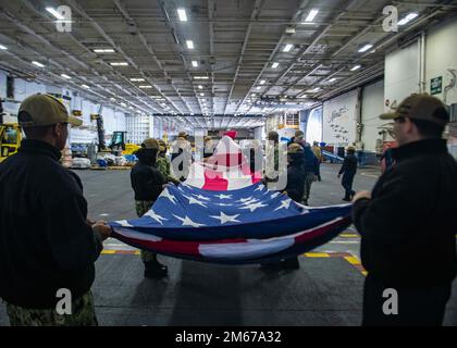 220411-N-XK462-1043 MARINEBASIS KITSAP-Bremerton, Washington, (11. April 2022) Seeleute falten eine zeremonielle Flagge in der Hangarbucht des Flugzeugträgers USS Nimitz (CVN 68). Nimitz ist im Hafen und bereitet sich auf zukünftige Operationen vor. Stockfoto