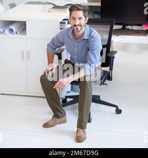 Er hat Erfolg. Porträt eines jungen Designers, der an seinem Arbeitsplatz in einem Büro sitzt. Stockfoto