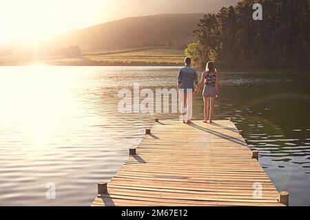 Liebe am See. Rückblick auf ein liebevolles junges Paar, das bei Sonnenuntergang auf einem Dock steht. Stockfoto