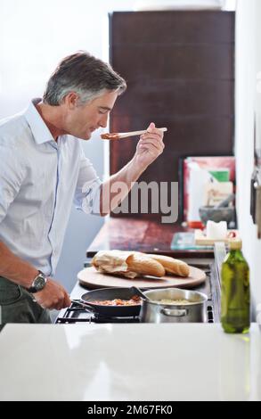 Das schmeckt wahnsinnig. Ein reifer Mann, der in der Küche kocht. Stockfoto