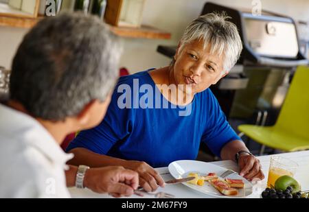 Genießt du das Essen? Ein glückliches Seniorenpaar, das ein gemütliches Frühstück zusammen zu Hause genießt. Stockfoto