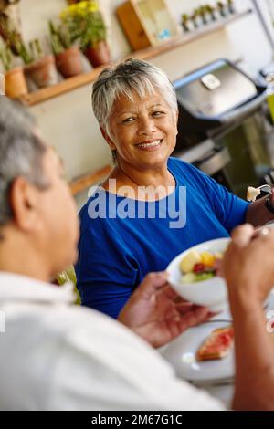 Genießen Sie ein entspannendes und gesundes Frühstück zusammen. Ein glückliches Seniorenpaar, das ein gemütliches Frühstück zusammen zu Hause genießt. Stockfoto