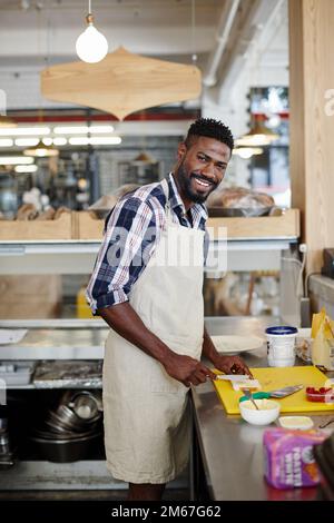 Wir servieren Kaffee und köstliche Sandwiches. Gekürztes Porträt eines gutaussehenden jungen Mannes, der in der Küche seines Cafés Essen zubereitet. Stockfoto