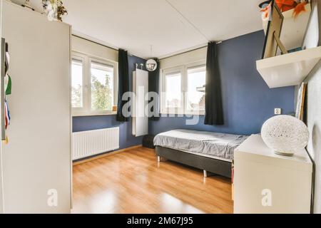 Ein Schlafzimmer mit blauen Wänden und Holzfußboden, einschließlich eines kleinen Bettes in der Ecke des Zimmers auf der rechten Seite ist ein Stockfoto