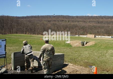 (Links) SPC. Amy Chen, ein Soldat des 2-104. General Support Aviation Bataillons, 28. Expeditionary Combat Aviation Brigade, wirft eine Scheingranate auf das Ziel im Graben, während der Granatenveranstaltung des Best Warrior Competition der Pennsylvania Army National Guard am 12. April 2022. Das Ziel in den Graben zu bringen, war eines von sechs verschiedenen Szenarien, bei denen die Mitbewerber mit der richtigen Interaktion konfrontiert wurden Stockfoto