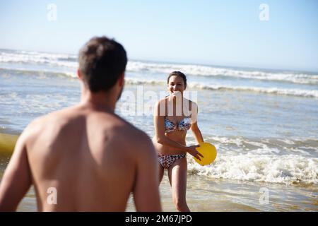 Bereit. Ein glückliches Paar, das im flachen Wasser am Strand mit einem Ball spielt. Stockfoto