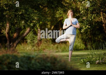 Sich in der Natur völlig entspannt zu fühlen. Eine attraktive Frau, die eine Yoga-Session in der Natur genießt. Stockfoto