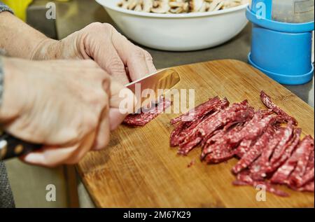 Der Koch schneidet Salami auf Holzbrett in der Küche Stockfoto