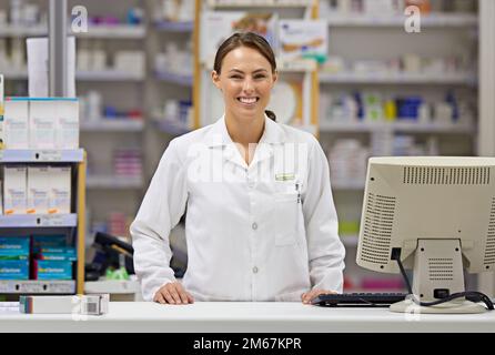 Wir halten unsere Kunden gesund und glücklich. Porträt eines attraktiven jungen Apothekers, der an der Rezepttheke steht. Stockfoto