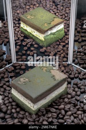 Hausgemachter Käsekuchen mit dunkler Schokolade Matcha und geröstete Kaffeebohnen mit Reflexion im Spiegel werden auf der schwarzen Acrylfolie präsentiert. Selektiv f Stockfoto