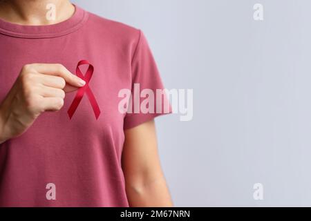 Burgundisches rotes Band für den März des Multiplen Myelom-Krebses und den Dezember des Welt-Aids-Tages-Bewusstseinsmonats. Konzept des Tages des Gesundheitswesens und des Weltkrebses Stockfoto