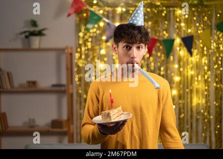 Ein komischer Kerl feiert zu Hause Geburtstag, hat Geburtstagskuchen in der Hand und trägt einen Partyhut, steht über goldenem Folienhintergrund