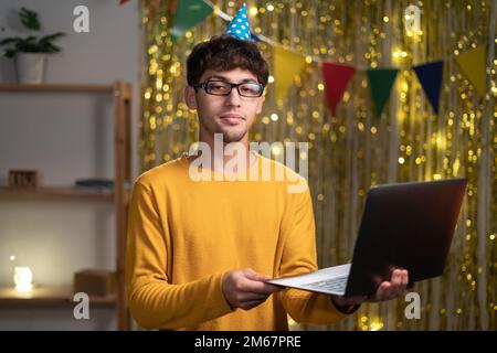 Lächelnder junger arabischer Mann 20s in Brille trägt einfachen, leichten Pullover mit Laptop-PC auf hellem, gelbem Hintergrund zu Hause Stockfoto