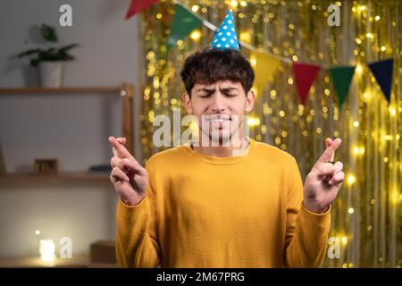 Porträt eines aufgeregten arabers, der sich wünscht, Daumen drücken für Glück an seinem Geburtstag, Augen schließen, alles tun, um zu beten, um zu träumen flehen Stockfoto