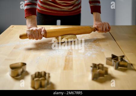 Eine unbekannte Frau rollt Ingwerteig mit einer Nadel auf dem Küchentisch aus Stockfoto