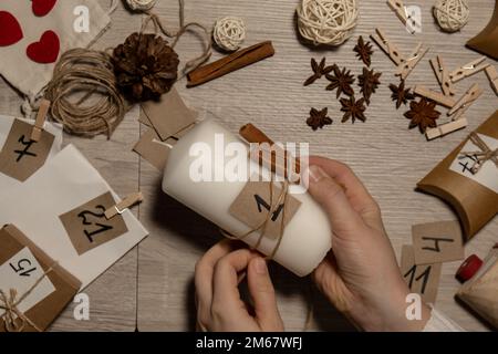 Eine nicht erkennbare junge Frau malt Zahlen auf Kerzen. Frau macht hausgemachte Adventskalender mit eigenen Händen gemacht Schritt für Schritt selbstgemachtes Kunsthandwerk Machen Sie es selbst. Vorbereitung auf das weihnachtskonzept. Saisonale Aktivitäten für Kinder, Familienurlaub im Winter. Umweltfreundlich Geschenke. Öffnen Sie das Paket jeden Tag Stockfoto