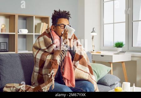 Ein kranker junger lateinamerikanischer Mann mit Brille fühlt sich unwohl, Schüttelfrost und laufende Nase. Stockfoto