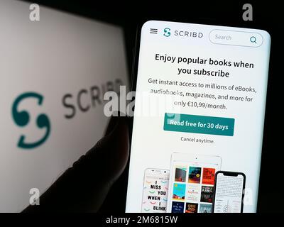 Person, die ein Mobiltelefon mit einer Webseite des US-Verlagsunternehmens Scribd Inc. Auf dem Bildschirm vor dem Logo hält. Konzentrieren Sie sich auf die Mitte des Telefondisplays. Stockfoto