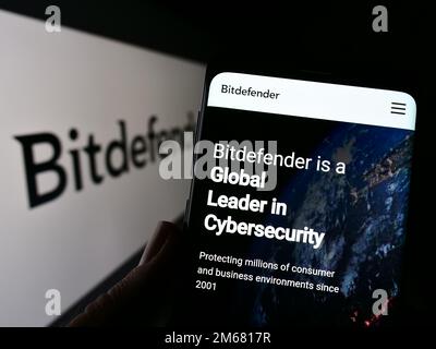 Person, die ein Mobiltelefon mit einer Website des rumänischen Cybersicherheitsunternehmens Bitdefender auf dem Bildschirm vor dem Logo hält. Konzentrieren Sie sich auf die Mitte des Telefondisplays. Stockfoto