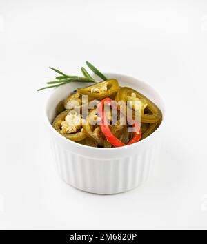 Heiße Jalapeno-Paprika, in eine weiße Schüssel geschnitten, mit Rosmarin auf isoliertem Hintergrund. Traditioneller mexikanischer Gemüsesnack. Stockfoto