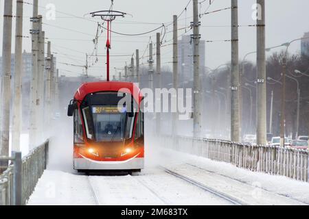 Die rote Straßenbahn rauscht während eines Schneesturms in der Stadt Stockfoto