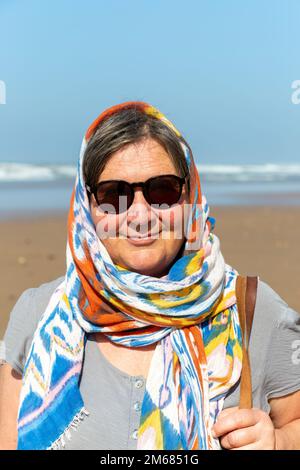 Frau mittleren Alters am Strand mit Sonnenbrille und Kopftuch, Marokko, Nordafrika - Modell veröffentlicht Stockfoto