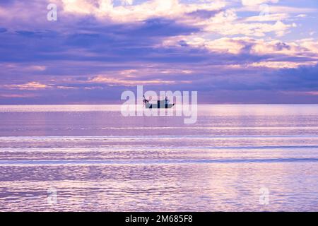 Ein kalter Tag in Troon Schottland, wenn die Sonne hinter dem Horizont untergeht, und ein Angelboot in der Bucht mit ausgestreckten Netzen Stockfoto