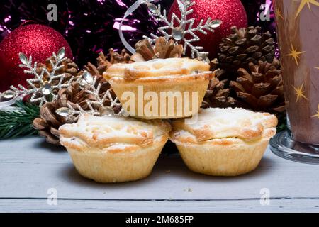 Drei frisch zubereitete weihnachtskuchen, umgeben von Dekorationen und einem Glas heißer Schokolade. Stockfoto