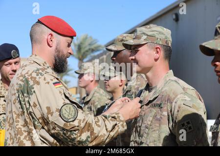 Major Christoph Hänsel, der stellvertretende hochrangige nationale Vertreter für Deutschland, stiftete während einer Verleihung der Auszeichnung der deutschen Streitkräfte auf der Basis der Union III Forward Operating Base in Bagdad, Irak, am 15. April 2022 ein US-Soldat mit dem Abzeichen der deutschen Streitkräfte. Das deutsche Bundeswehrabzeichen wird an Soldaten vergeben, die in der Kampfkunst befähigt sind, und ist ein offizieller Militärpreis, der nur von eingesammelten Wehrmitgliedern getragen werden darf. AdviseAssistEnable, StrongerTogether, Stockfoto
