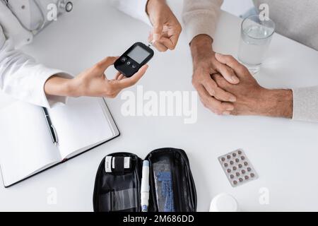 Draufsicht eines afroamerikanischen Arztes zeigt Glukometer und Teststreifen für Patienten mittleren Alters, Stock-Bild Stockfoto
