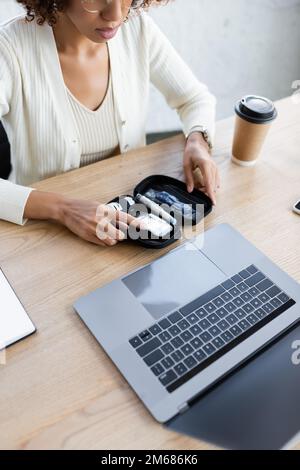 Freigestellte Ansicht einer afroamerikanischen Geschäftsfrau, die ein Diabetes-Kit in der Nähe eines Laptops und Kaffee im Büro hält, Bild von Stock Stockfoto