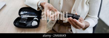 Freigestellte Ansicht einer afroamerikanischen Geschäftsfrau, die ein Glukometer in der Nähe des Diabetes-Kits im Büro hält, Banner, Stockbild Stockfoto