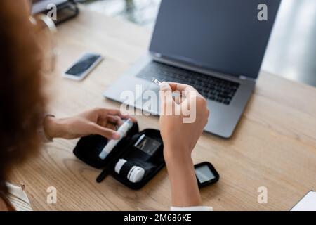 Zugeschnittener Blick auf eine afroamerikanische Geschäftsfrau, die einen Teststreifen mit Lanzettenstift im Büro hält, Stockbild Stockfoto