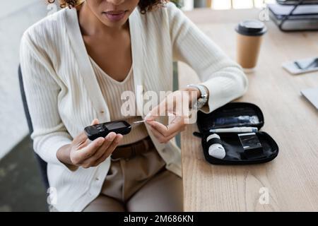 Freigestellte Ansicht einer afroamerikanischen Geschäftsfrau, die ein Glukometer im Büro hält, Aktienbild Stockfoto