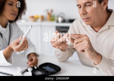 Lockiger afroamerikanischer Arzt, der einen Lanzettenstift in der Nähe eines Patienten mittleren Alters mit Diabetes hält, Stock Image Stockfoto