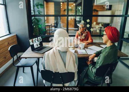 Ethnische Geschäftsfrauen, die an einem virtuellen Meeting in einem modernen Büro teilnehmen. Multikulturelle Geschäftsfrauen, die eine Videokonferenz mit ihrem Unternehmen veranstalten Stockfoto