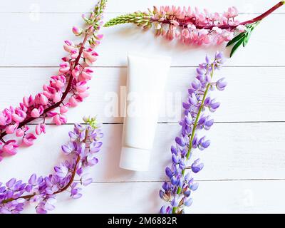 Beauty Spa medizinische Hautpflege und Kosmetiklotion Flasche Creme Verpackung Produkt und Lupinen Blumen auf weißem Holztisch. Draufsicht. Blumenmuster flach liegend, li Stockfoto