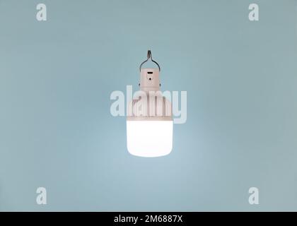 Tragbare, wiederaufladbare USB-LED-Notleuchte mit integriertem Akku auf blauem A-Hintergrund. Lichtquelle bei Stromausfall. Minimalistische Zusammensetzung. Stockfoto