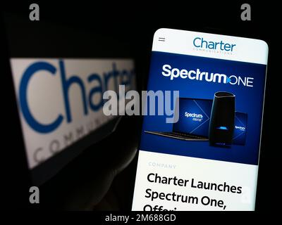 Person, die ein Mobiltelefon mit einer Webseite des US-Medienunternehmens Charter Communications Inc. Auf dem Bildschirm mit Logo hält. Konzentrieren Sie sich auf die Mitte des Telefondisplays. Stockfoto