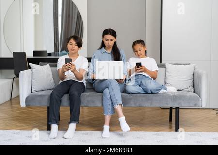 Frau benutzt Laptop in der Nähe asiatischer Kinder mit Smartphones zu Hause, Stock Image Stockfoto