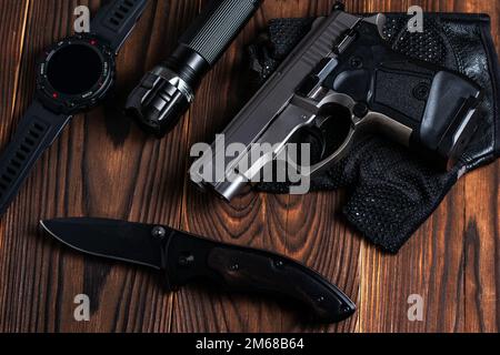 Klappbares Taschenmesser mit Pistole und Taschenlampe auf Holzhintergrund, Stockfoto