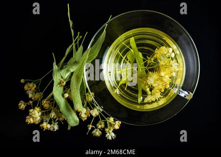 Eine Tasse Kräutertee mit Lindenblumen auf schwarzem Hintergrund. Stockfoto