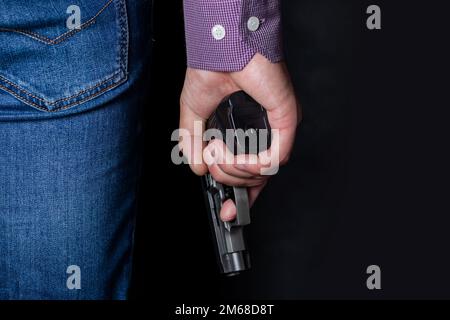 Ein Mann, der hinter seinem Rücken eine Waffe in der Hand hält, Nahaufnahme. Konzepte: Verbrechen, versuchter Mord, eine Schusswunde, der Mörder, Raub Stockfoto