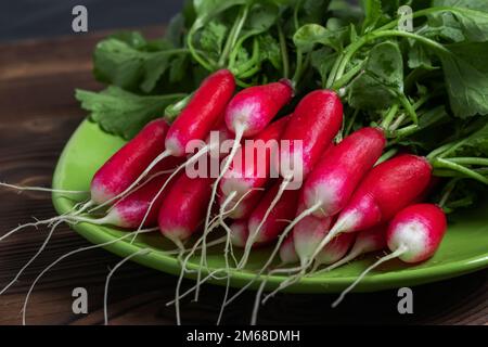 Im Sommer geernteter roter Rettich. Anbau von Bio-Gemüse. Ein großer Haufen roher, frischer, saftiger Rettich auf dunklen Brettern, bereit zum Essen Stockfoto